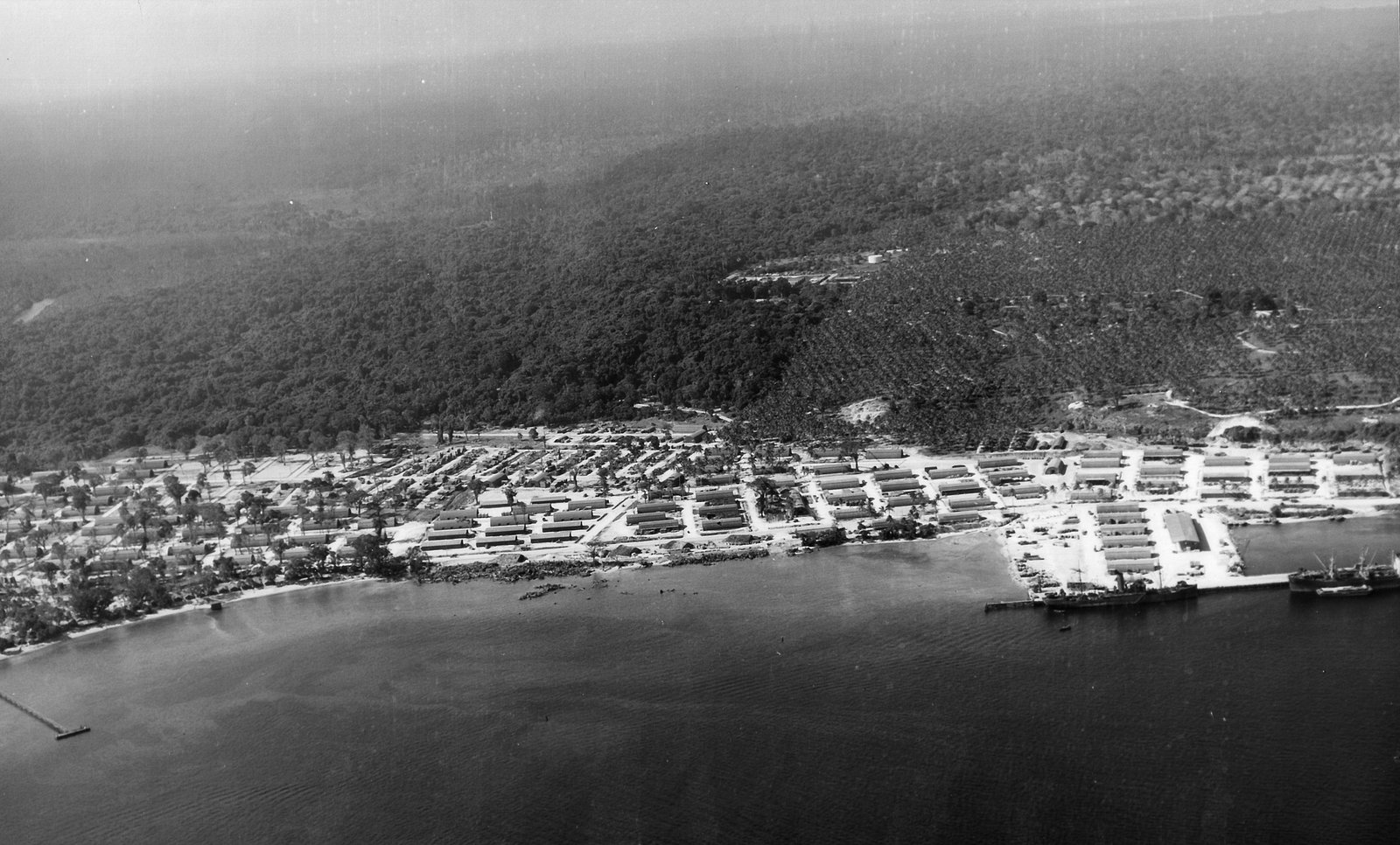 Aerial view of Santo Base with rows of buildings along the coast and lush jungle.