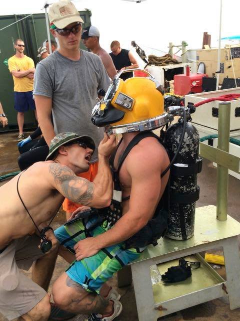 Divers prepare for a dive, one wearing a yellow helmet and scuba gear
