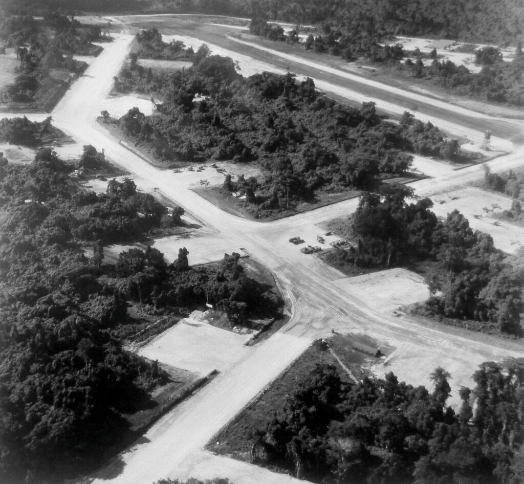 Aerial view of a jungle airfield with multiple runways and parked aircraft.