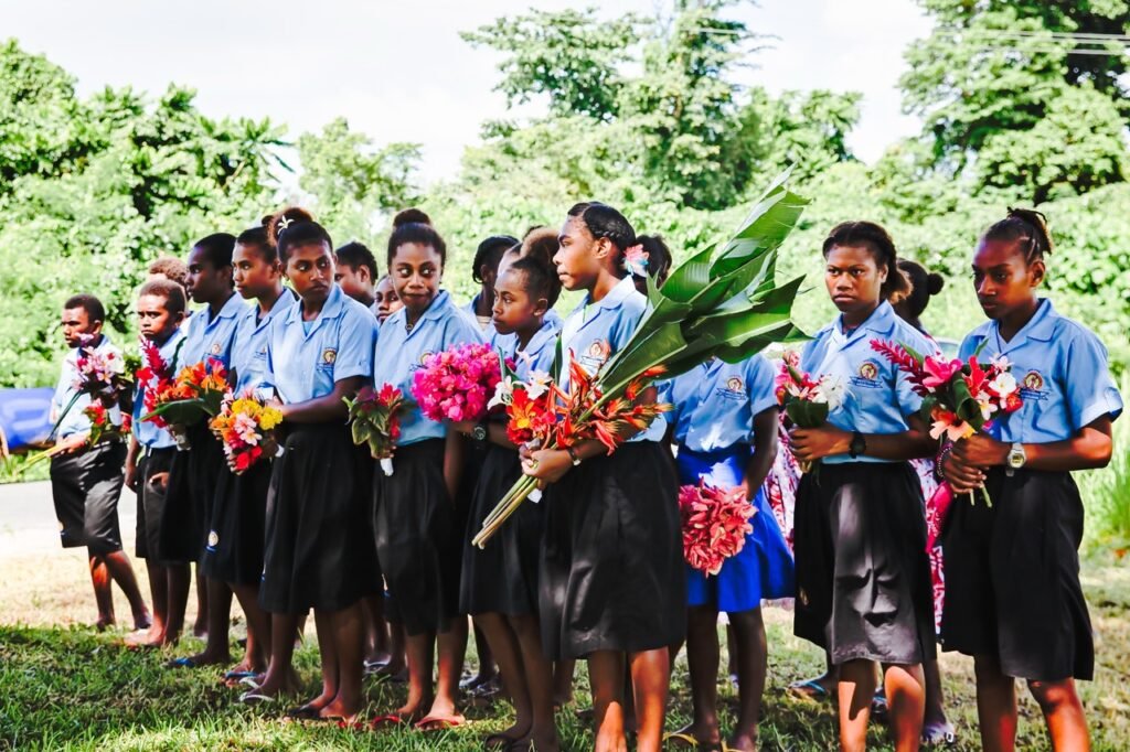 Students in blue shirts and black skirts hold flowers for Coolidge Commemoration event.