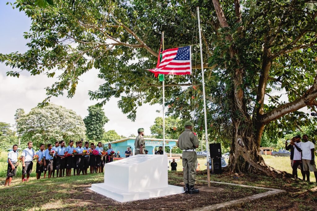 Commemoration ceremony with flags, people, and a monument.
