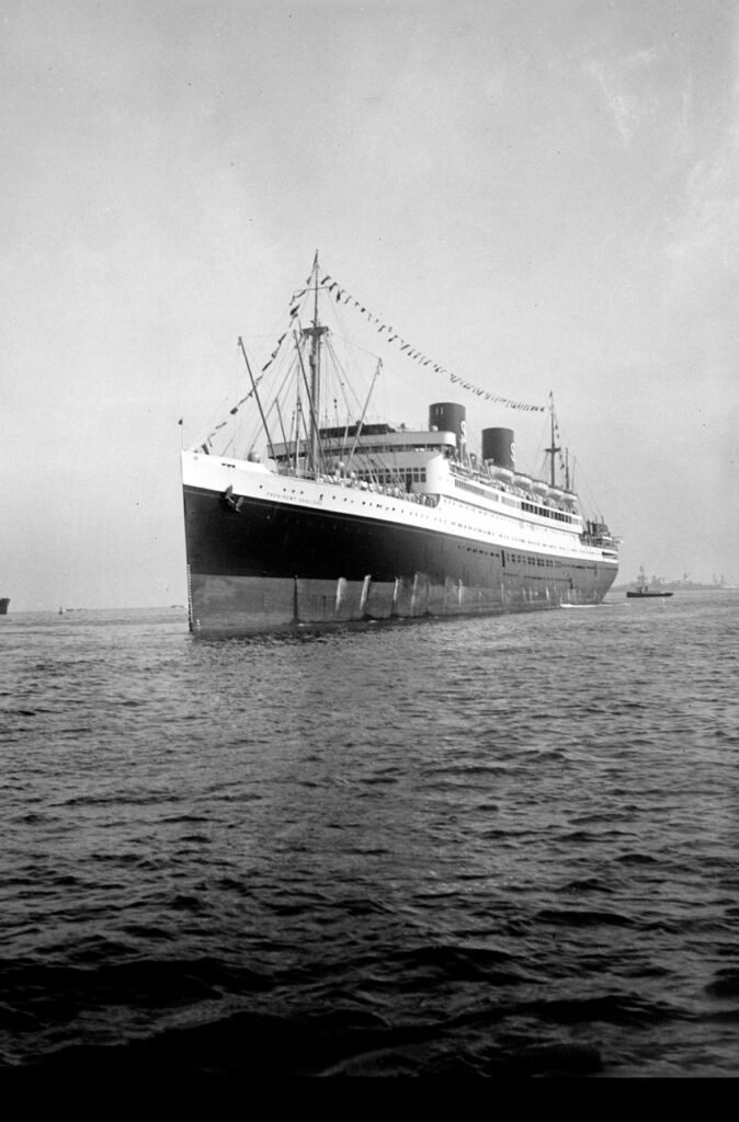 The Queen Mary ocean liner, decorated with flags, sails at sea.