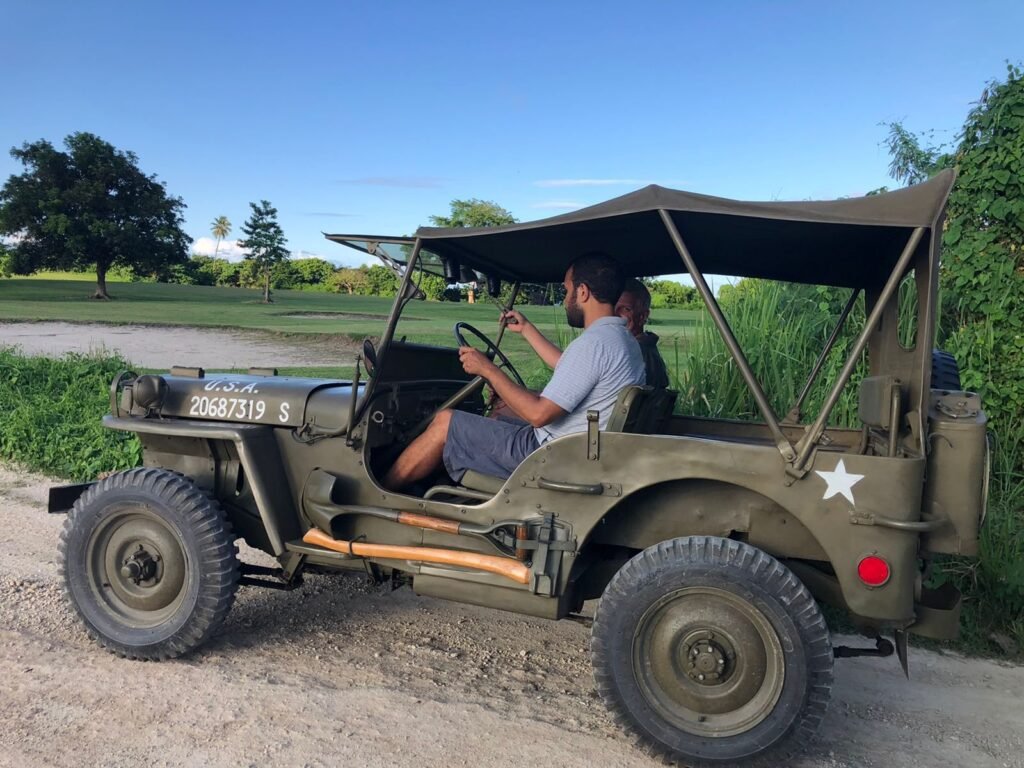 Two men in a vintage U.S. Army Jeep with "U.S.A. 20687319 S" on the side.