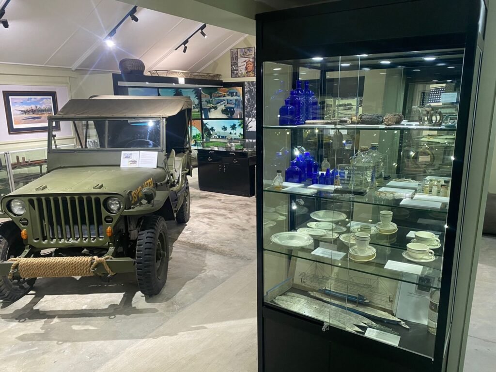 Museum exhibit: vintage green jeep and display case with artifacts.