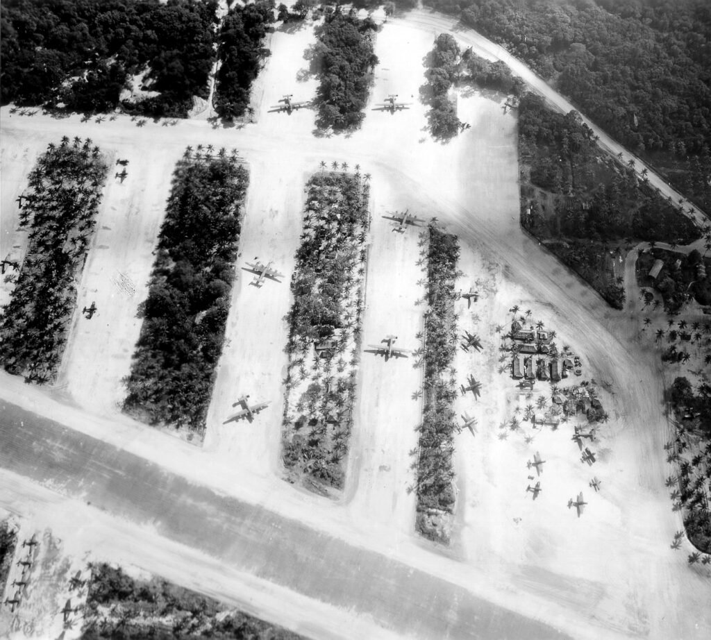 Aerial view of a World War II airfield with parked airplanes and palm trees.