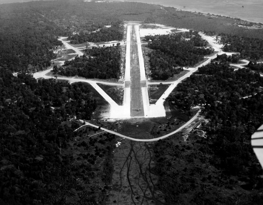 Aerial view of a jungle airfield with a single airplane on the runway.
