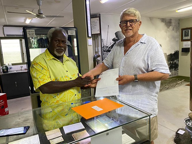 Two men shake hands over a counter, one holding a check.