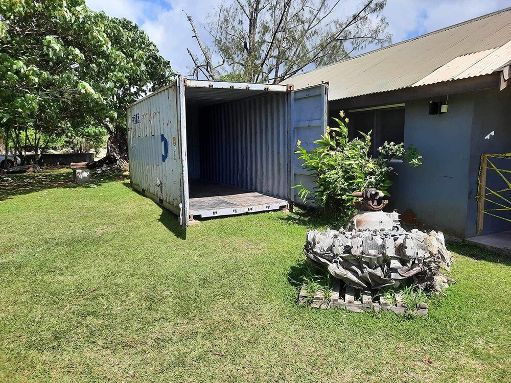 Open shipping container and aircraft engine part on grassy lawn near building