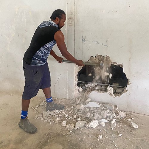 Man breaking hole in wall with sledgehammer, construction work