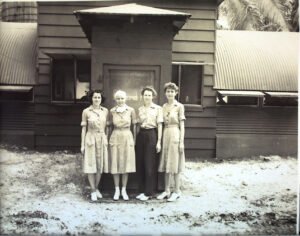 Four women in uniform stand in front of a wooden building, possibly from the 25th Division.