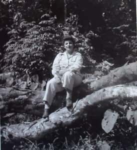 Woman sitting on a fallen tree trunk in a lush forest, historical photo.
