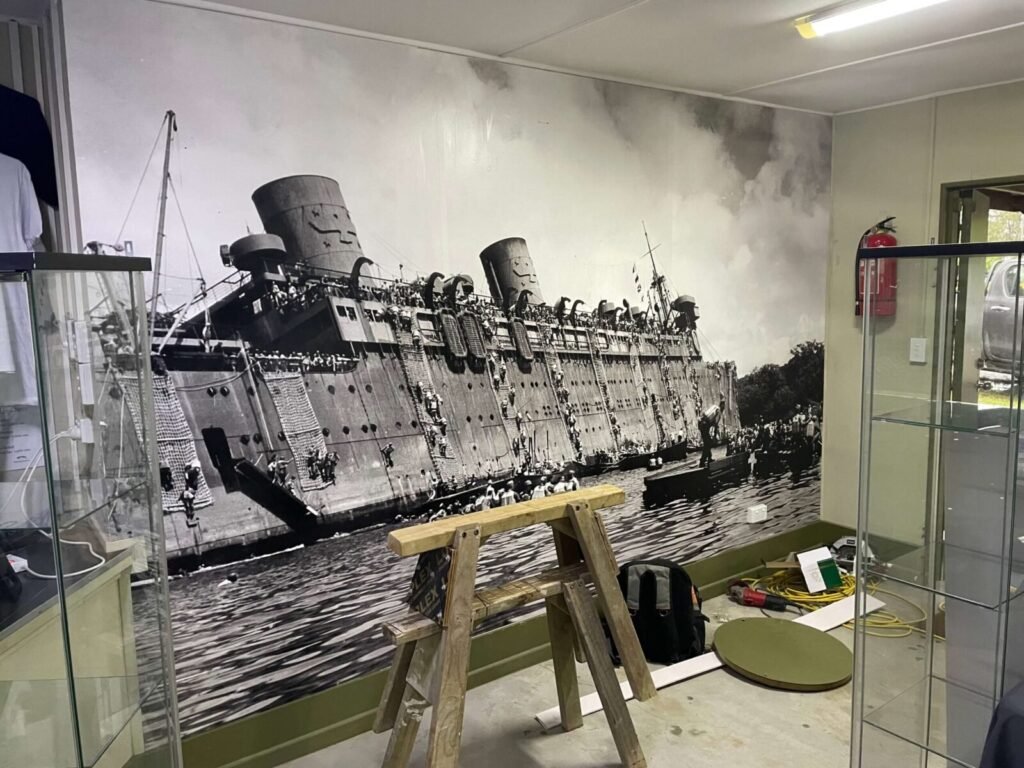 Large mural of a historic ship with crowds on deck, in a room with display cases.