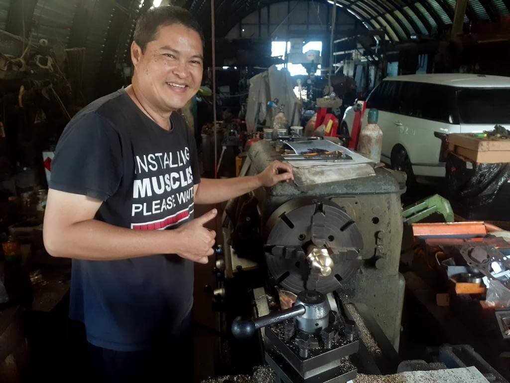 Man in a workshop with a lathe, wearing a t-shirt that says "INSTALLING MUSCLE PLEASE WAIT