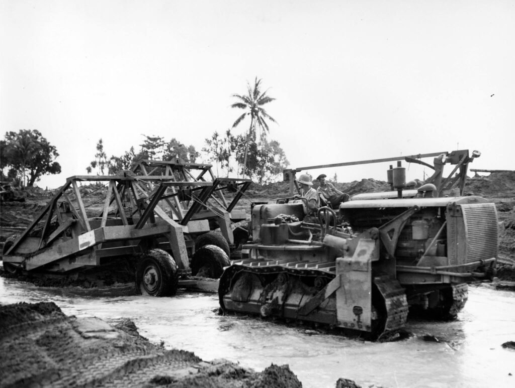 Bulldozer towing a large trailer through muddy terrain, likely related to Million Dollar Point.