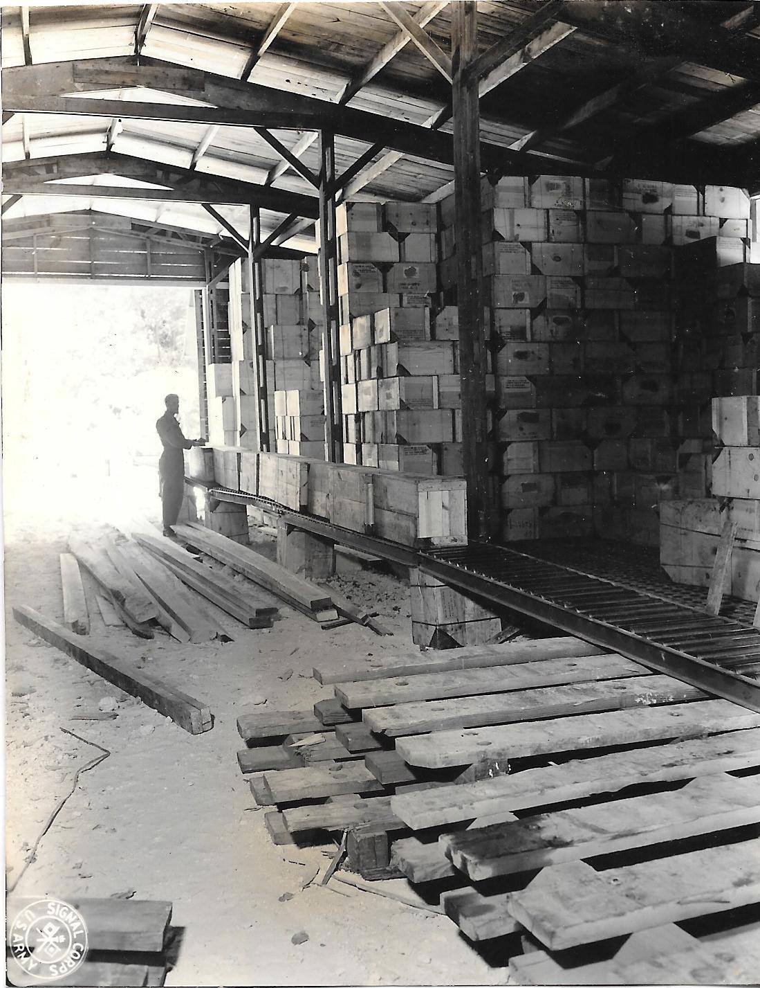 Man in warehouse with stacks of crates and lumber, possibly Million Dollar Point.