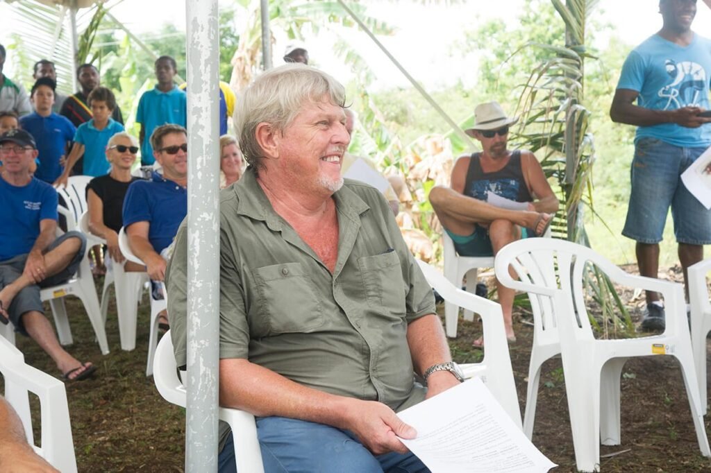 Man in green shirt speaking at outdoor event with attendees