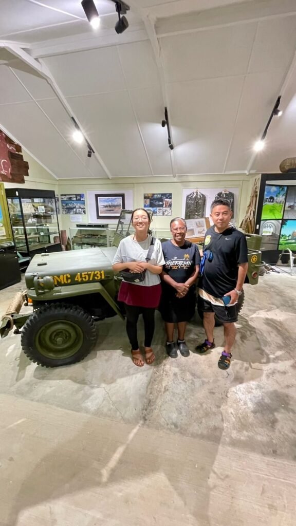 Three people pose in front of an olive green military jeep with "MC 45731" on the side.