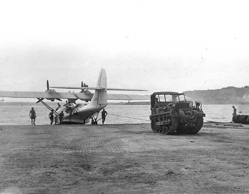 Seaplane being towed by a tracked vehicle on a concrete airfield.