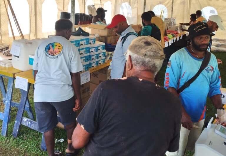 Men at a distribution event in a tent, receiving supplies.