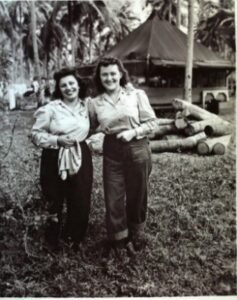 Two women in military uniforms stand outside a tent in a tropical setting, possibly related to the 25th Infantry Division.