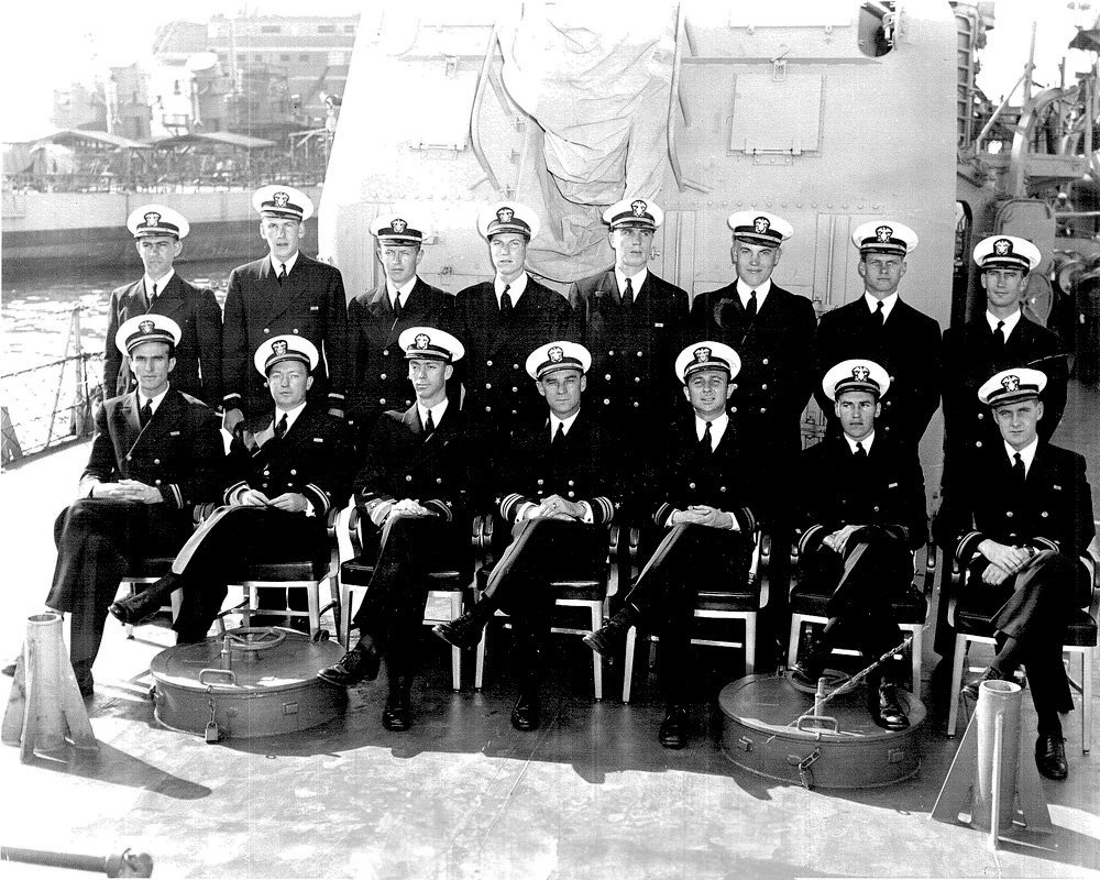 Group photo of 12 US Navy officers in uniform on a ship deck.
