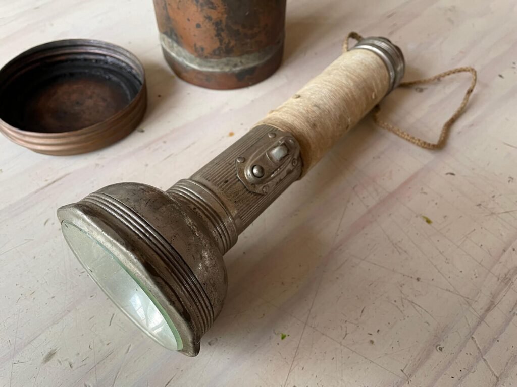 Antique flashlight with glass lens, copper lid, and twine-wrapped handle.