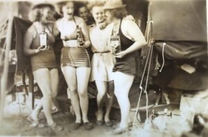 Four women in vintage swimwear celebrating with drinks, possibly from a 25th event.
