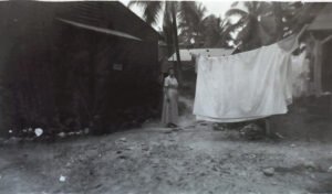 Woman in dress stands by dark building with laundry drying in the 25th.