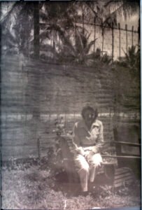 Woman sitting on a bench in a tropical garden, possibly celebrating a 25th anniversary.