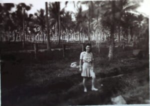 Woman in a tropical setting with palm trees, possibly from the 25th era.