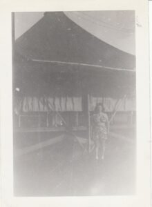 Vintage photo of a woman standing in front of a large tent, possibly from the 25th historical context.