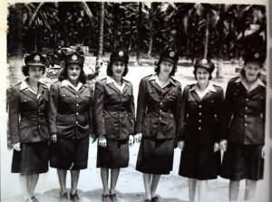 Six women in US Army uniforms, likely from WWII, stand in a line outdoors.