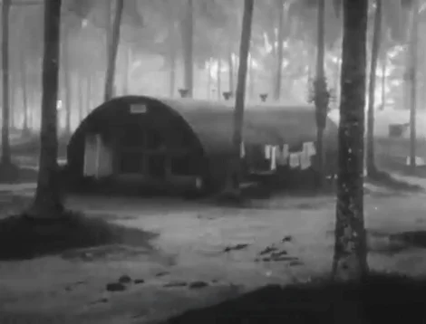 Quonset hut barracks in a tropical forest setting with laundry hanging to dry.